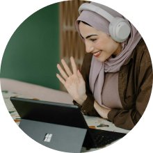 A woman with headphones in front of a tablet smiling and waving